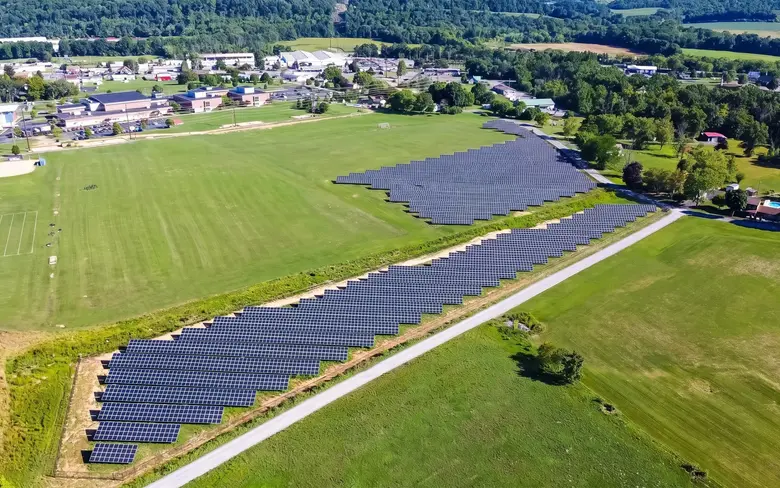 A ground-mounted solar array beside a school's playing fields, seen from a drone